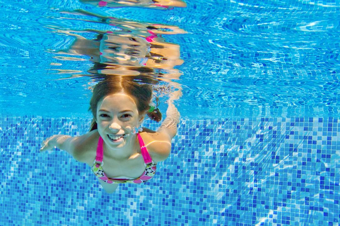 Happy child swims underwater in pool, fun on family vacation